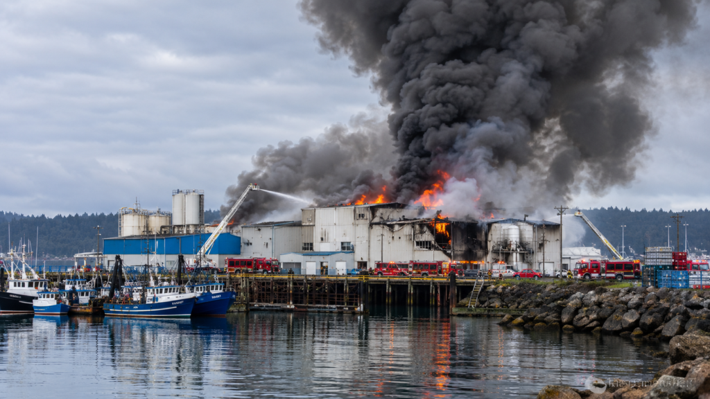 Illustration of Oregon seafood plant fire in Newport with thick smoke rising above an industrial waterfront facility